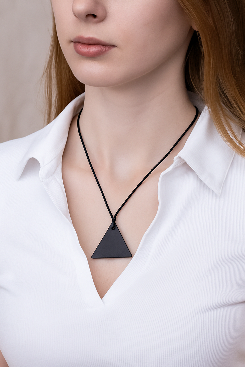 Shungite triangle pendant worn by a person, demonstrating its size, style, and everyday wearability as a natural EMF protection accessory.
